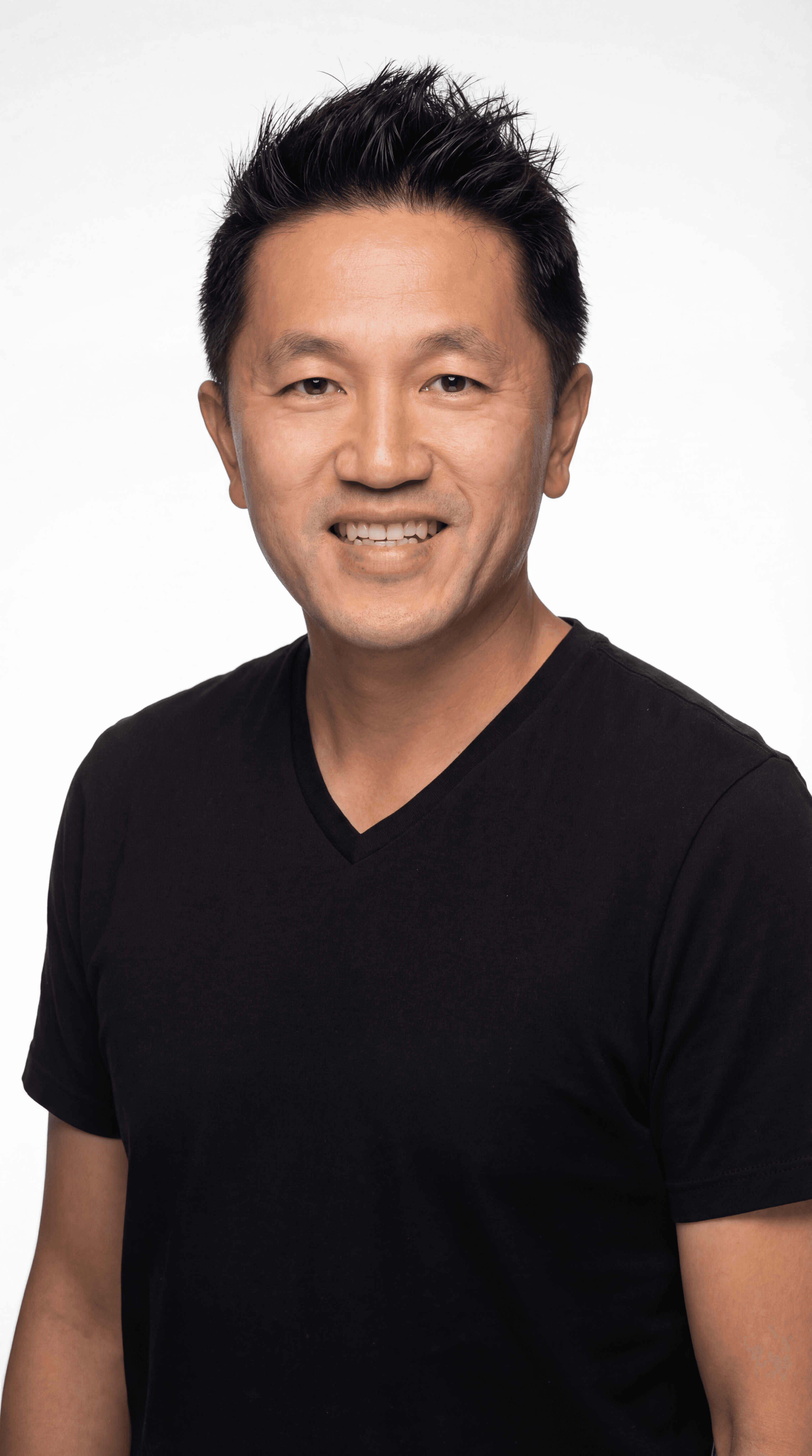 Smiling Asian man with spiky black hair in a black v-neck shirt, white background.